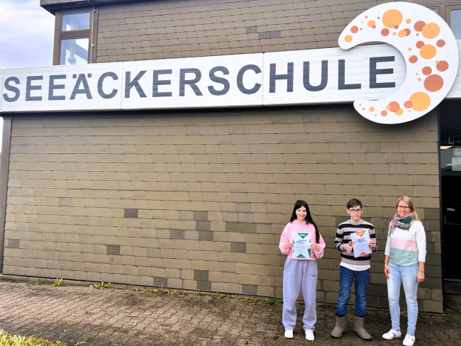 Die Schulsiegerin und der Zweitplatzierte mit ihren Urkunden und ihrer Lehrkraft Frau Kleesattel vor der Seeäckerschule.