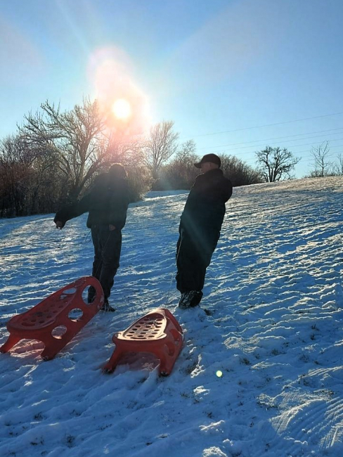 Zwei Schüler ziehen ihre Schlitten auf den Hügel.